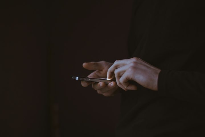 A person tapping on a phone held sideways against a dark background