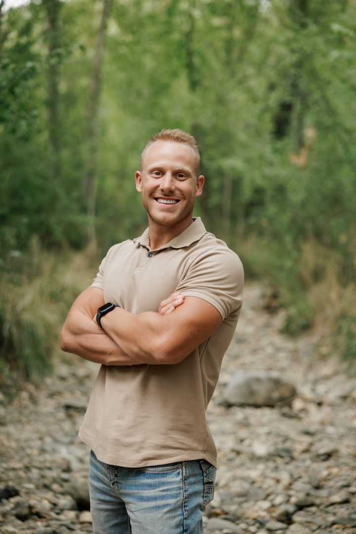Tate Strickland smiling with his arms crossed on a rocky trail lined with trees